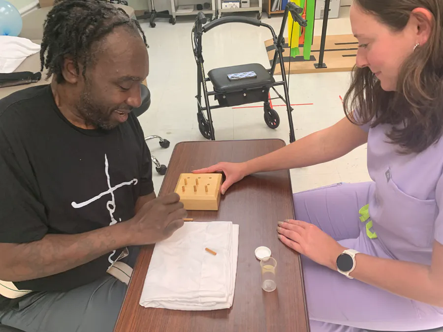 A male patient using a small peg board with a therapist.